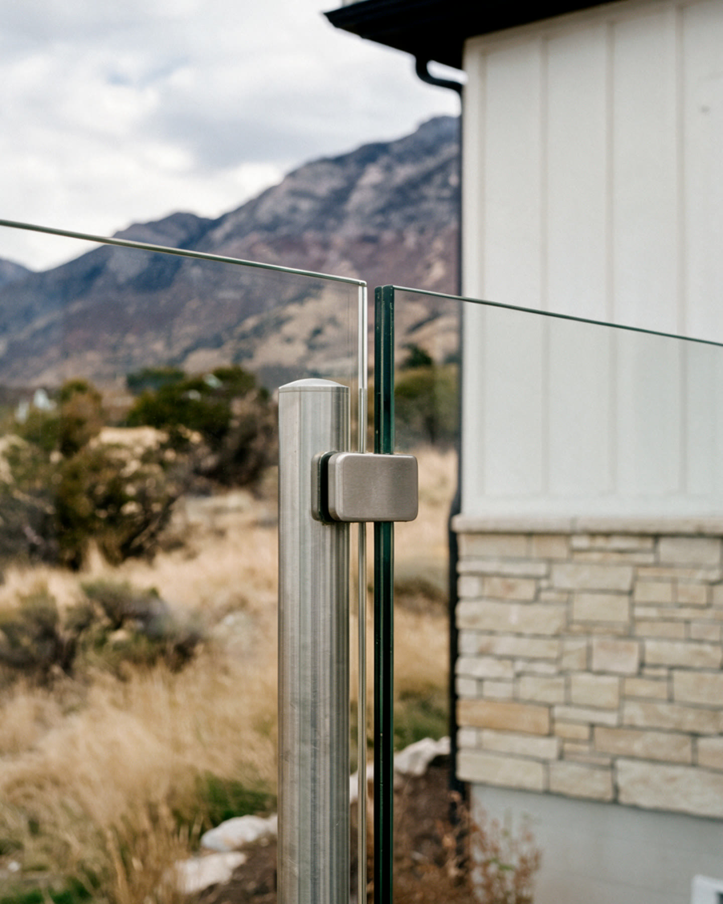 Frameless tempered glass deck railing held by a brushed stainless post, Wasatch foothills behind