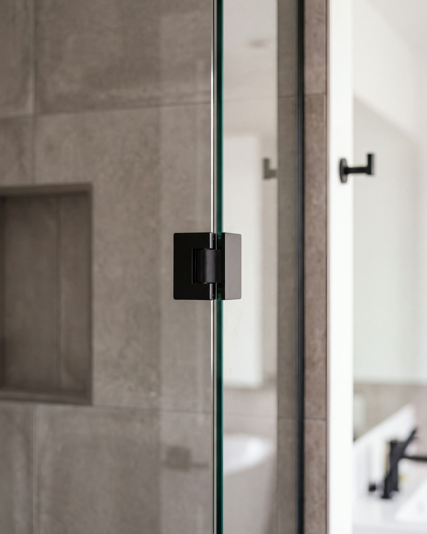 Close view of a frameless glass shower panel meeting its matte black hinge, stone-look tile behind