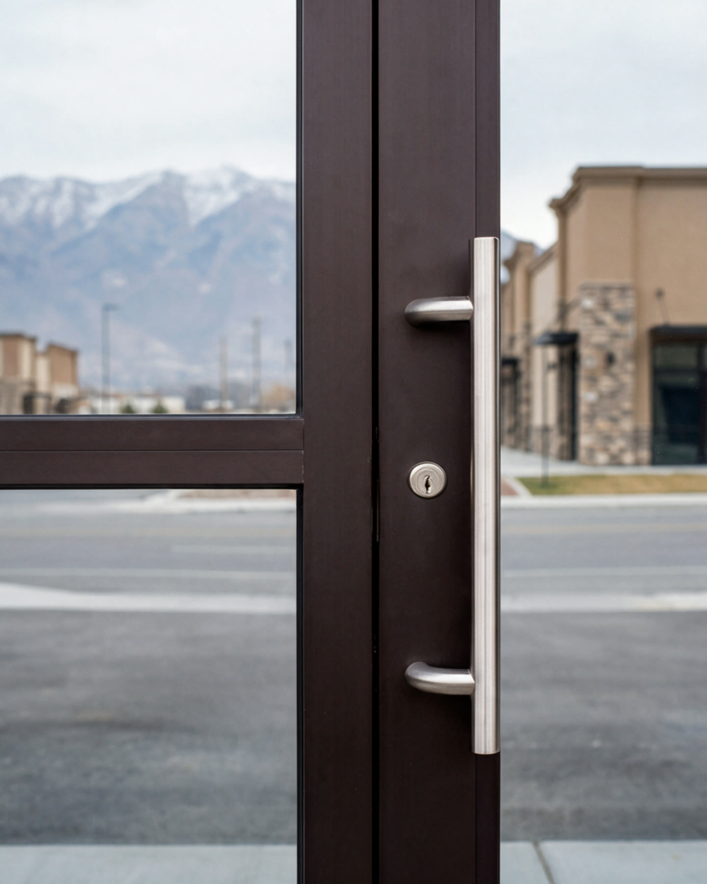 Dark bronze aluminium storefront door with a brushed steel pull handle, snow-topped Wasatch peaks beyond